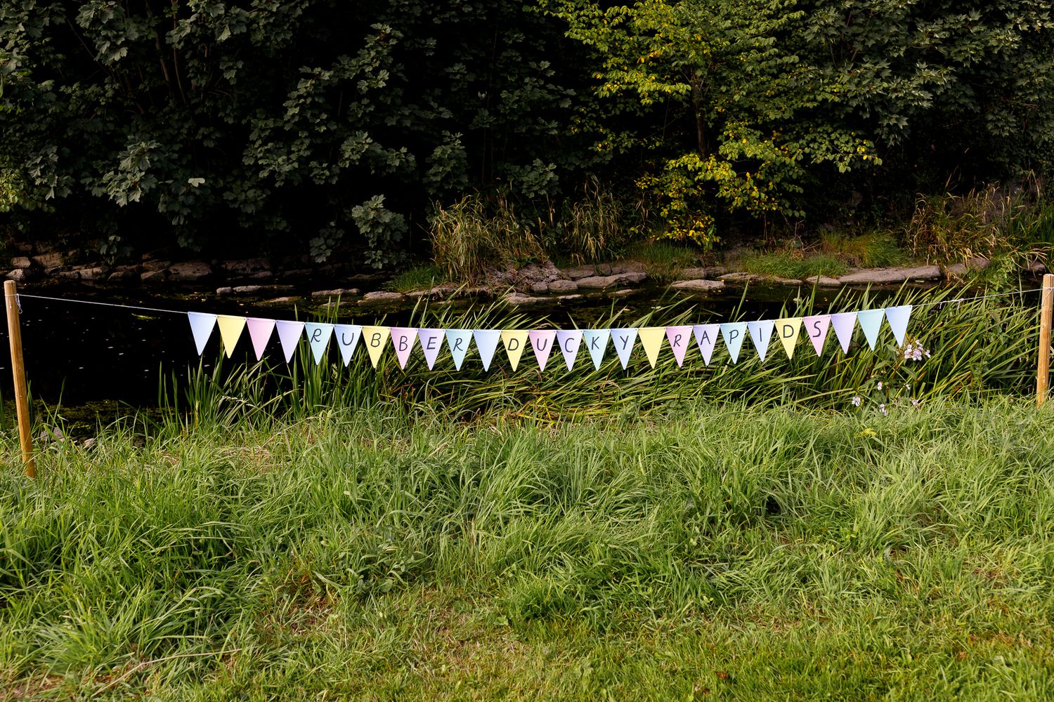 A rustic outdoor wedding venue with white bunting decorations strung between trees in a lush green garden setting.