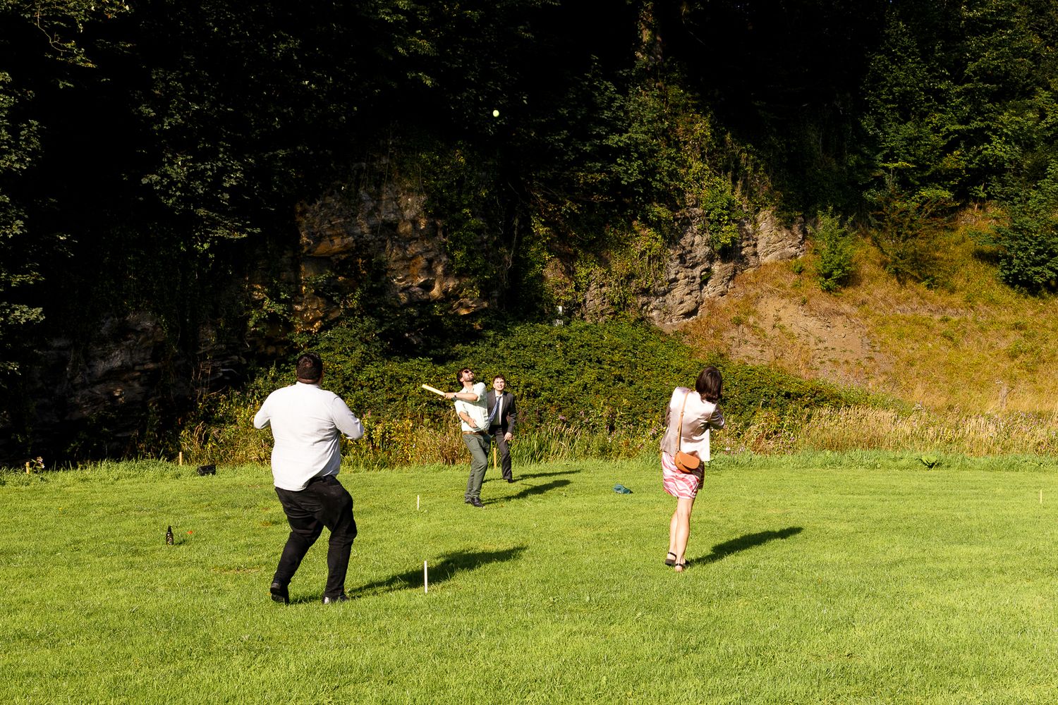 People walking on a grassy slope in a forest setting with shadows cast on the green meadow.