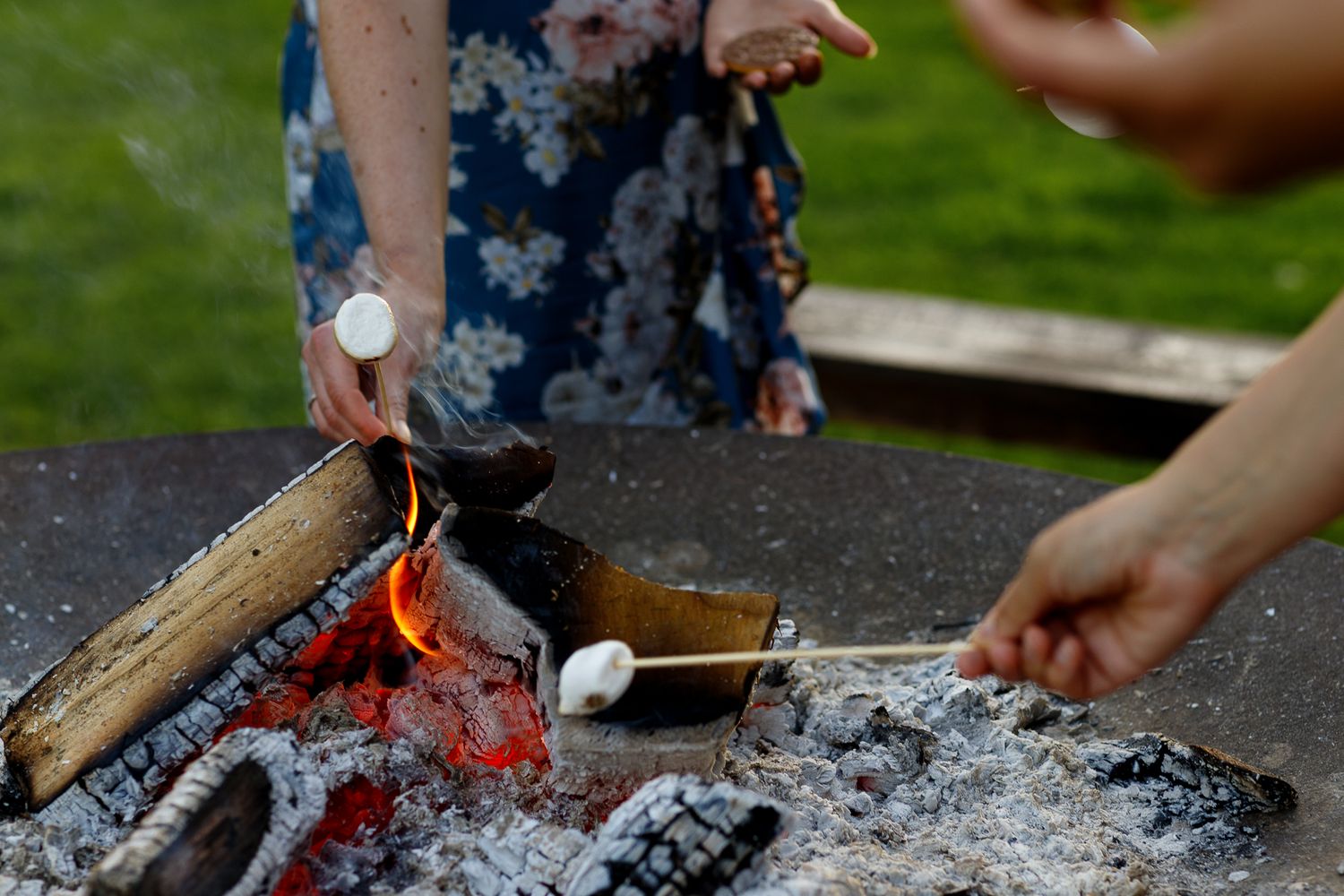 Close-up view of hands roasting marshmallows over a campfire with glowing embers in the background.