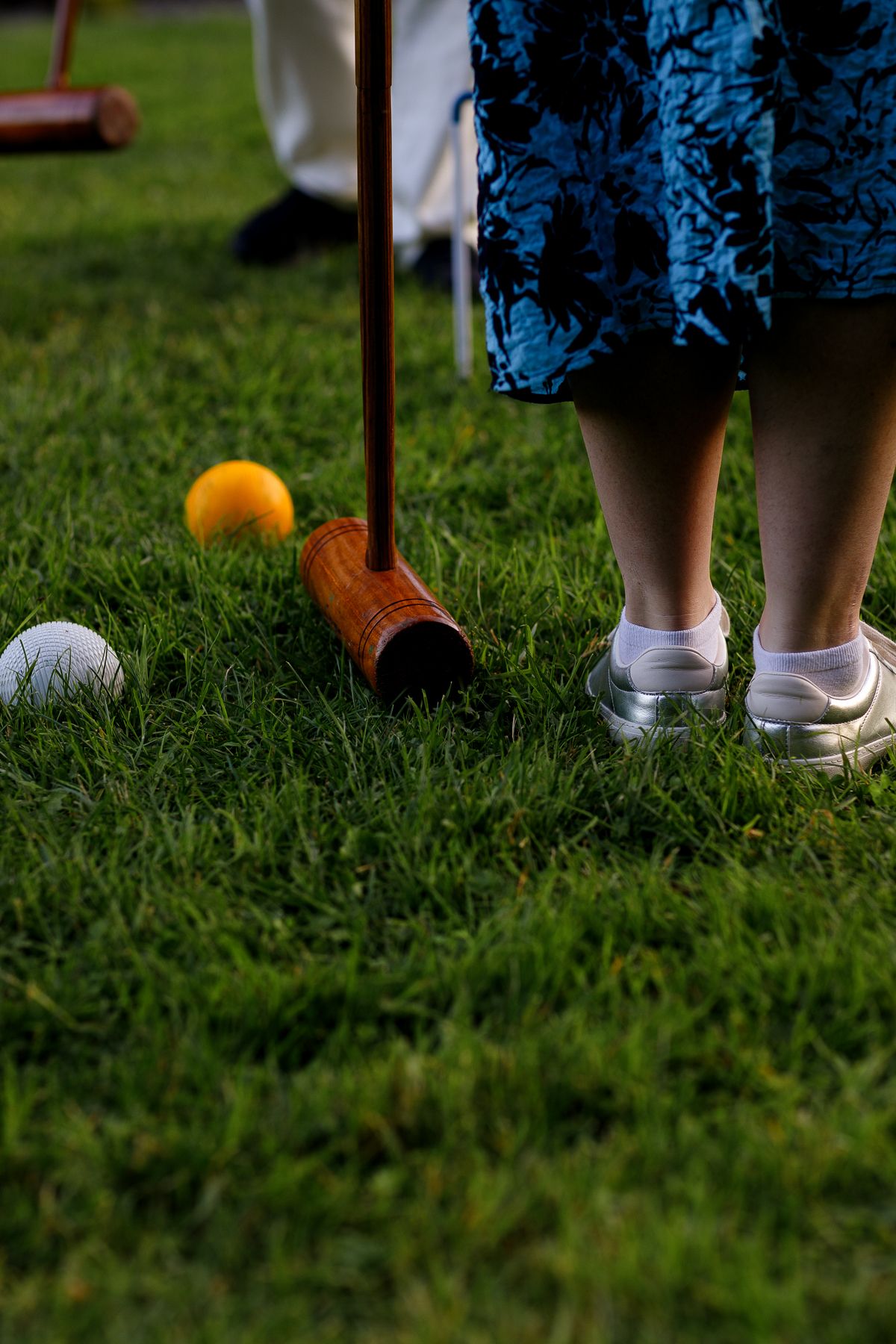 Feet wearing sneakers stand on green grass lawn during a croquet game.