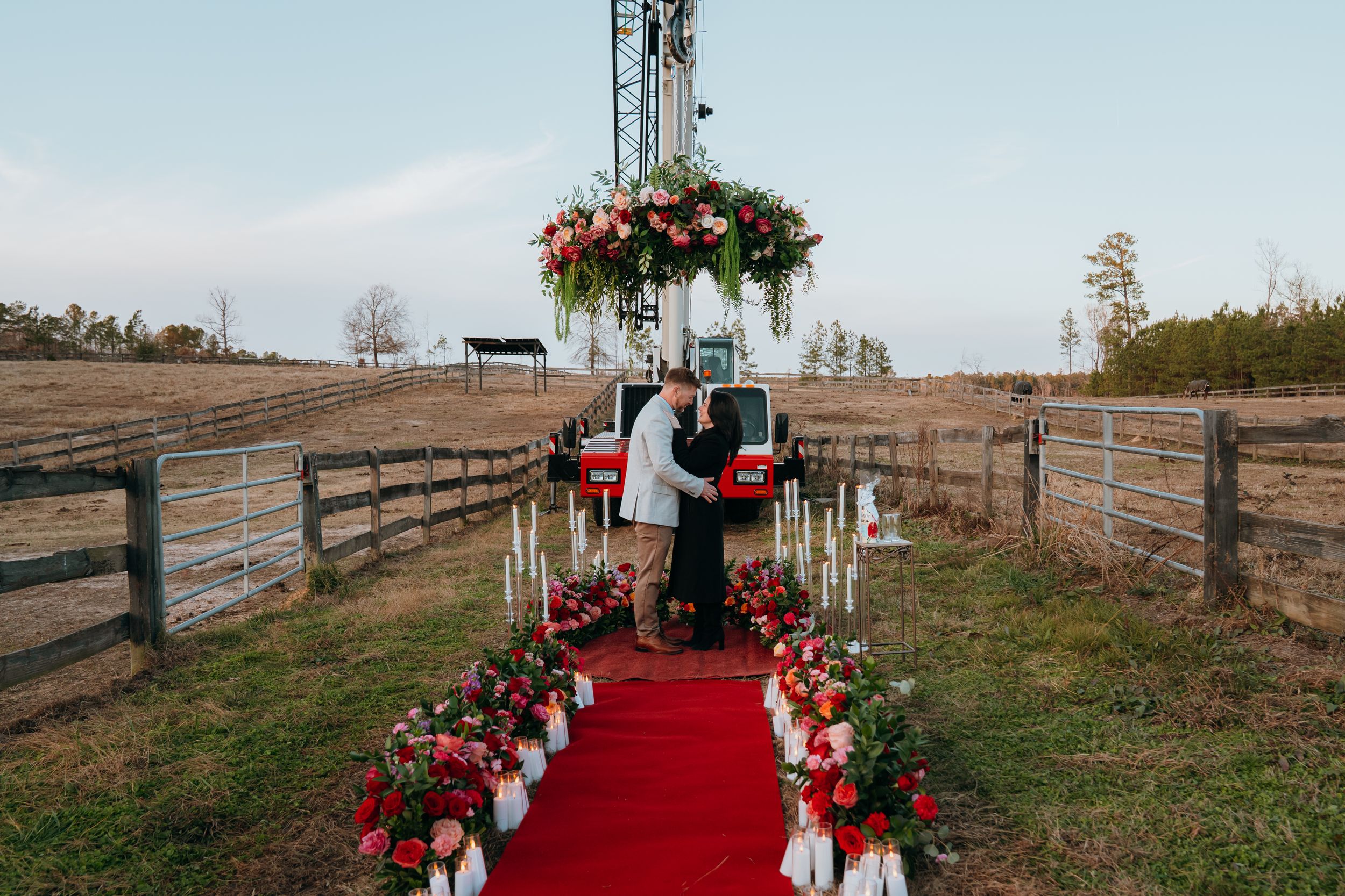 Outdoor wedding ceremony setup with a red carpet aisle runner leading to a wooden arch decorated with flowers.