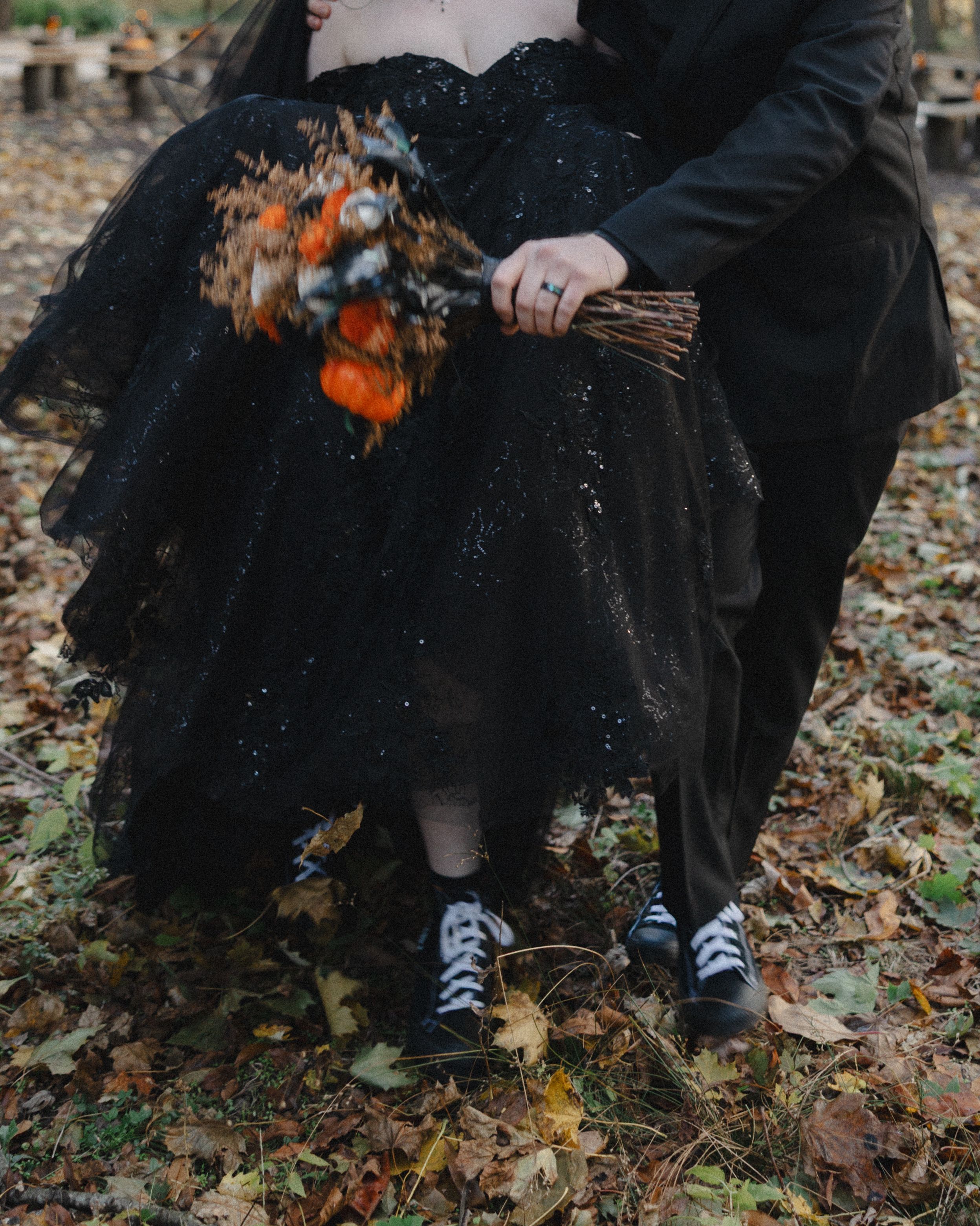 A person wearing black clothing and sneakers sits on fallen autumn leaves in an outdoor setting.