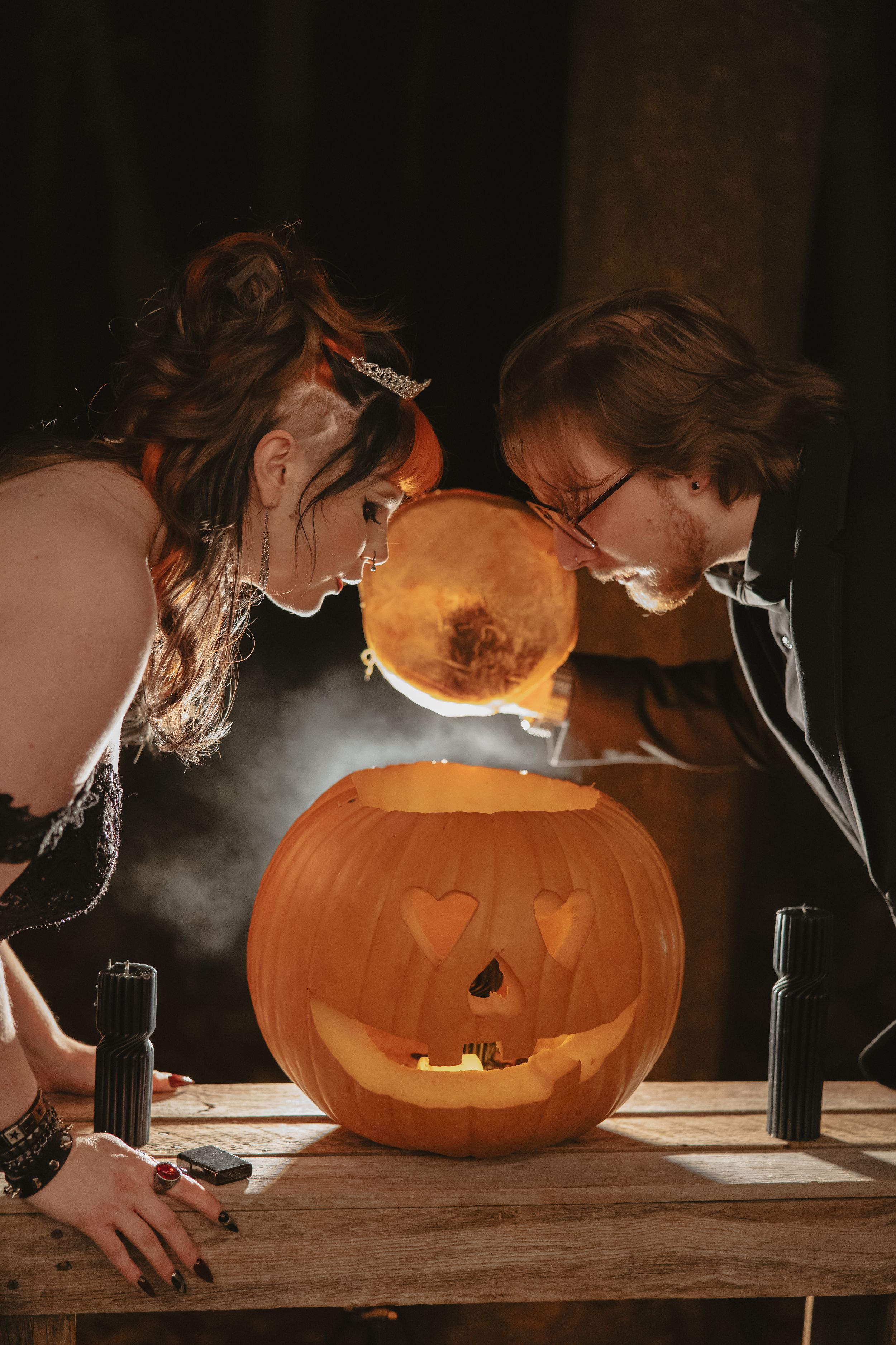 Person carving a Halloween pumpkin in dramatic lighting with smoke effects creating a spooky atmosphere.