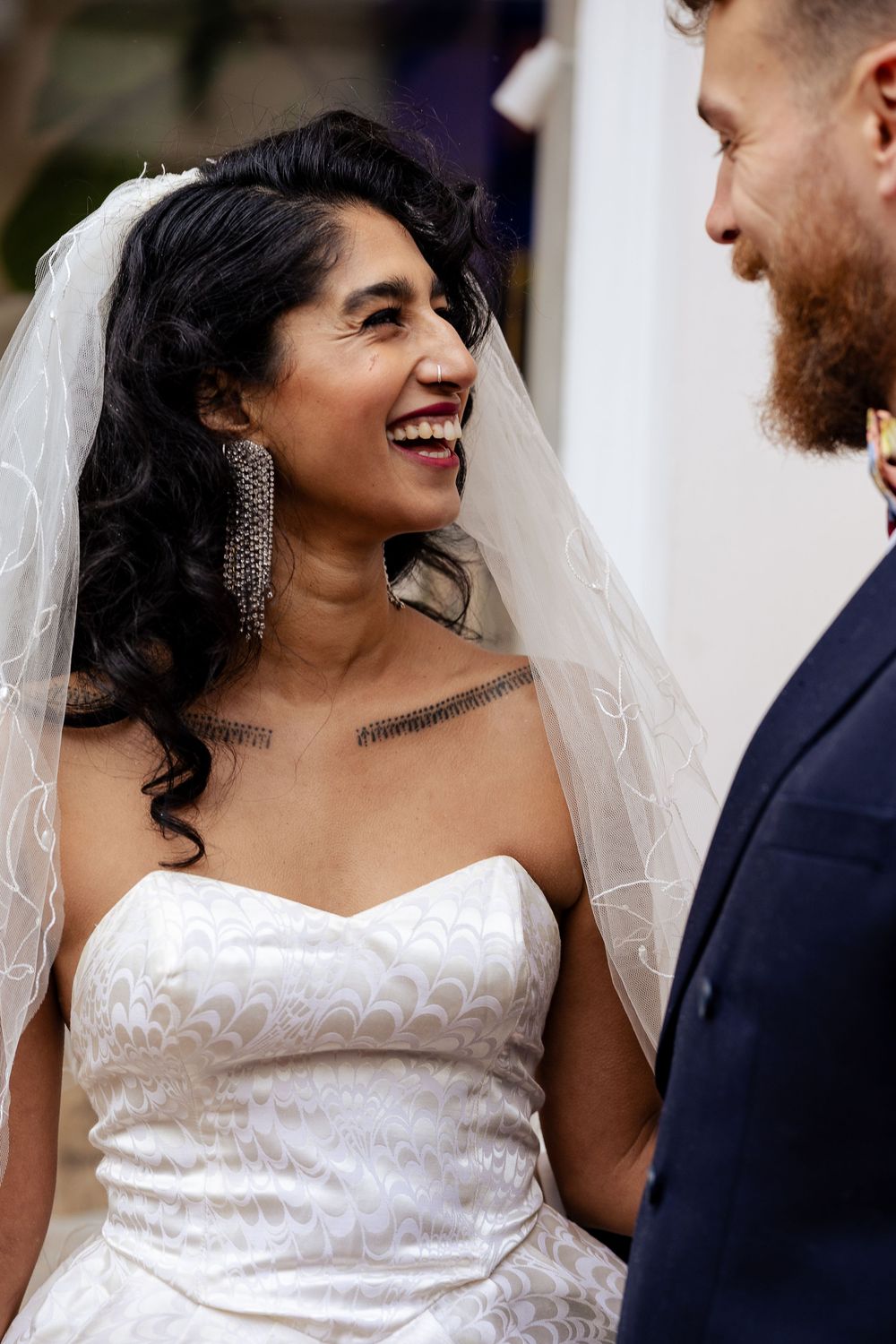 A bride in a white strapless wedding dress laughs joyfully while interacting with someone in a navy suit.