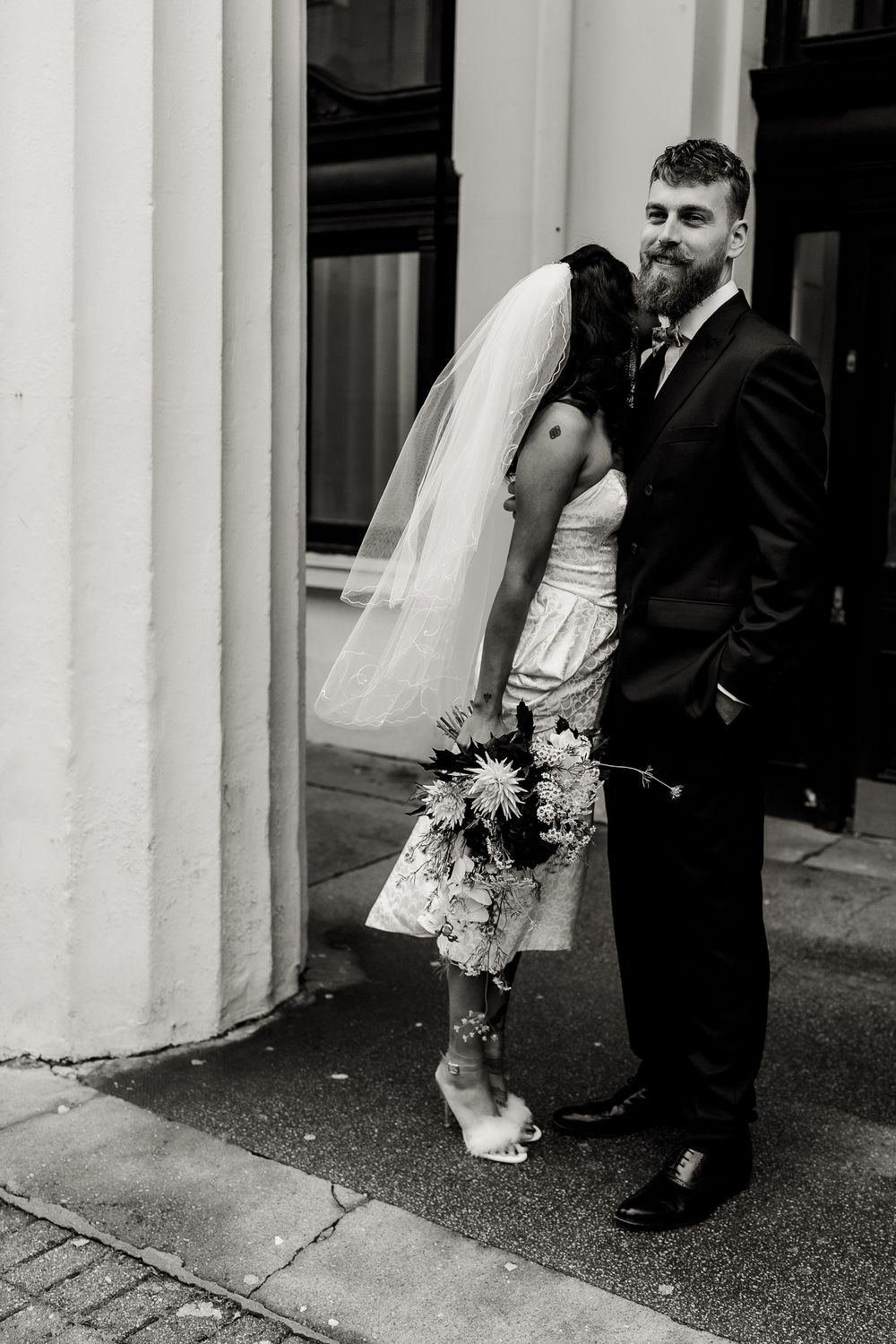 A series of romantic black and white wedding photos showing a couple's feet and dress details against white columns.