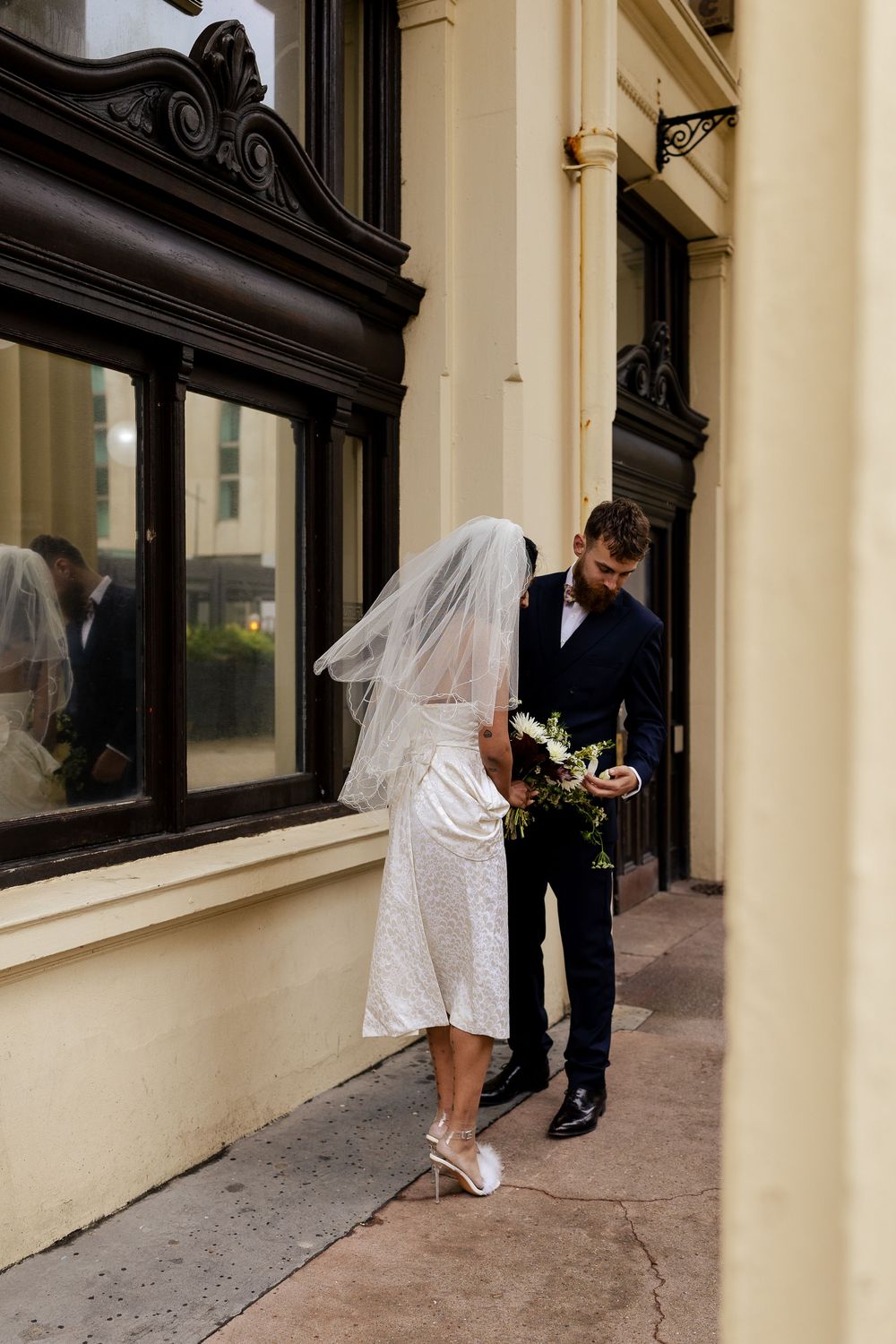 Wedding couple poses together against a classic architectural backdrop with cream colored walls.
