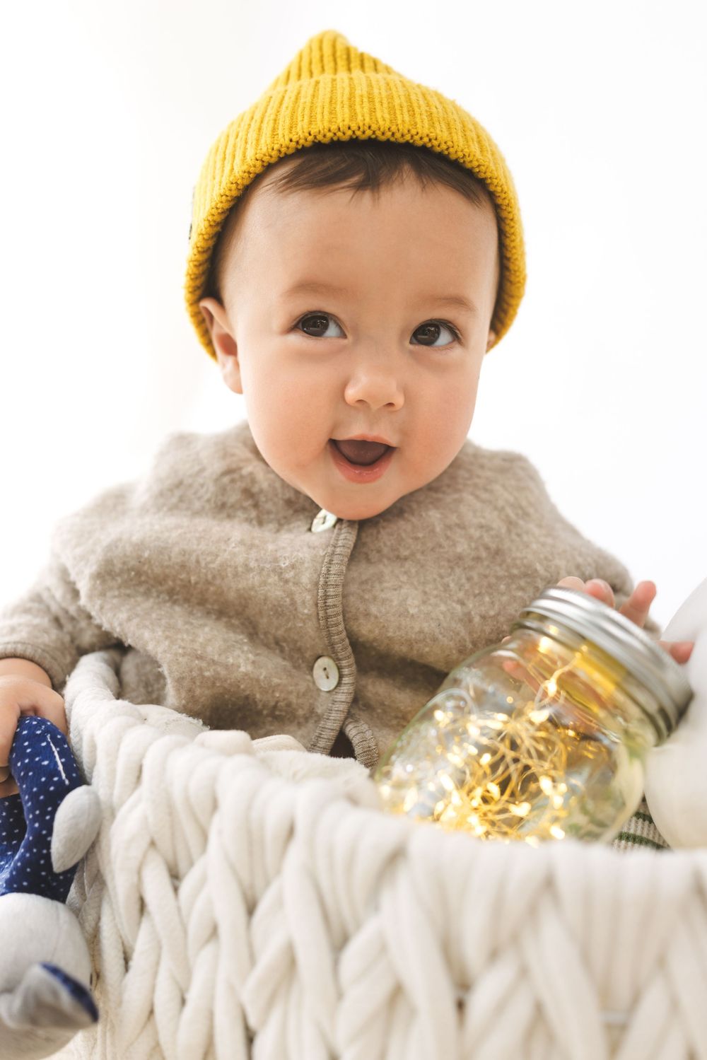 Baby wearing yellow beanie and gray sweater lying on chunky knit blanket in multiple poses.