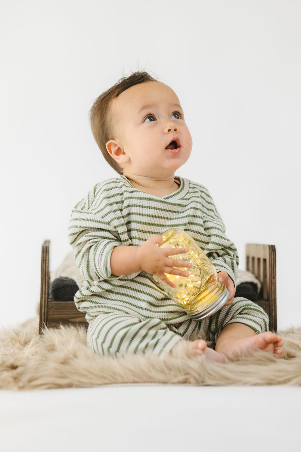 Baby in striped onesie sitting on soft blanket playing with string lights in three sequential photos.