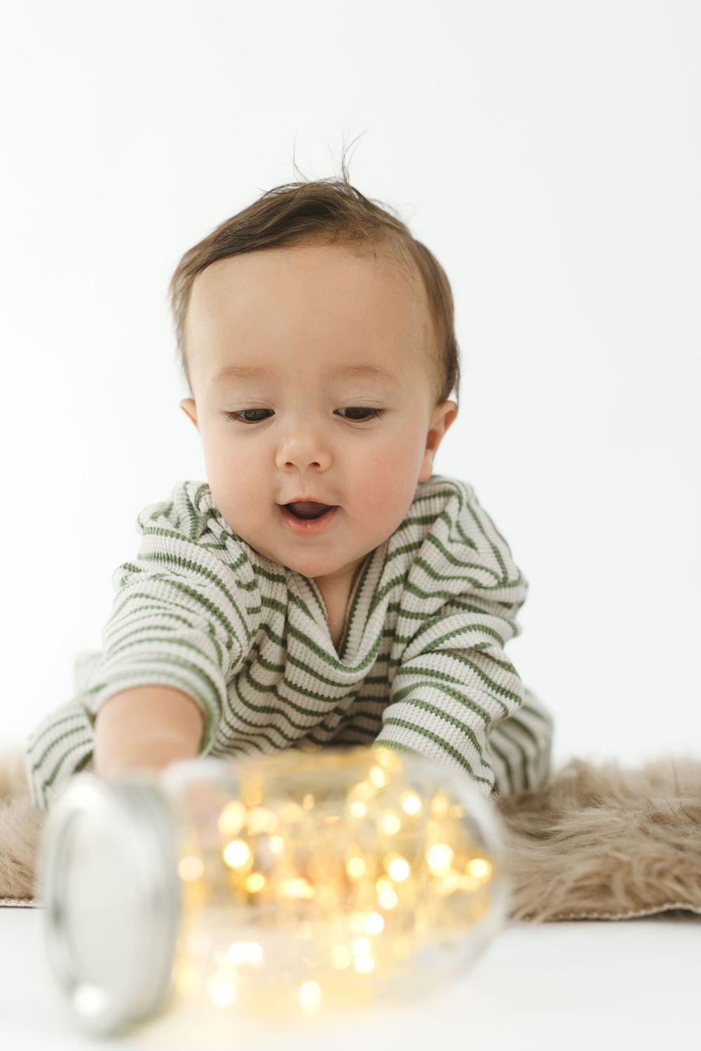 Baby in striped outfit lying on white surface with glowing string lights creating a magical atmosphere.