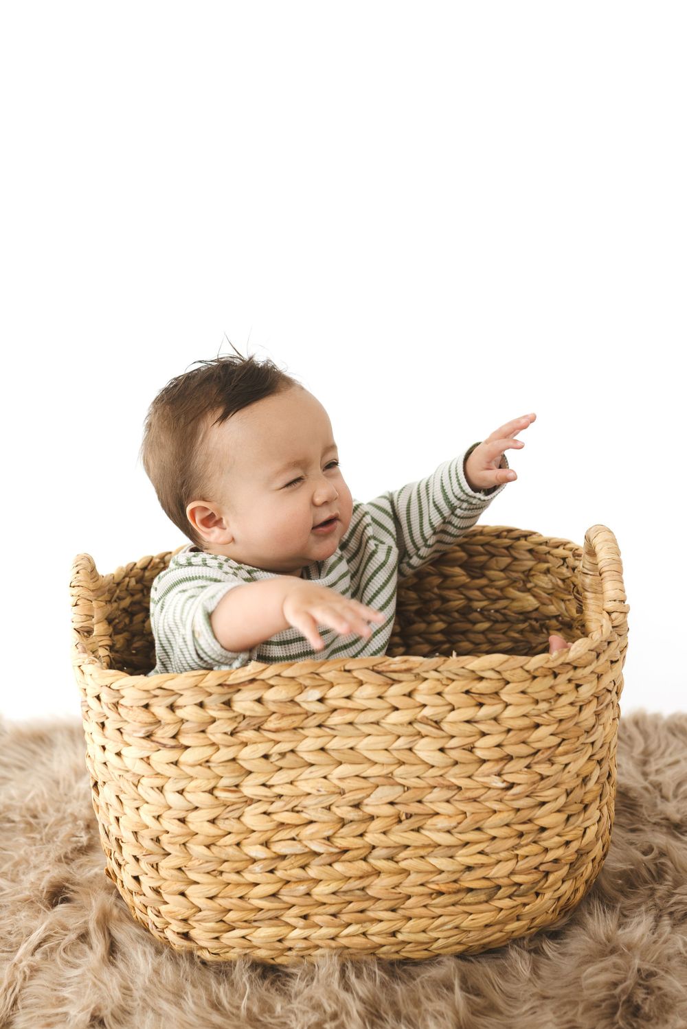 Three sequential photos show a baby lying in a woven basket on a furry rug, pointing and reaching outward.