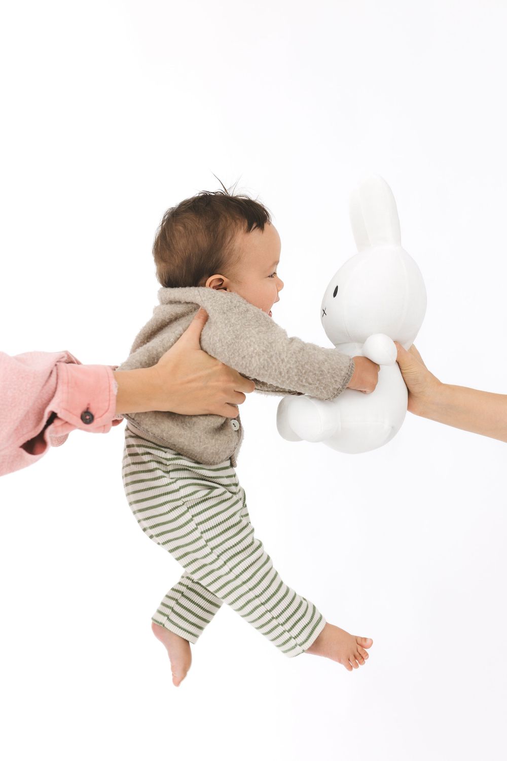 Baby in striped outfit sleeping peacefully while cuddling white stuffed animal on white background.