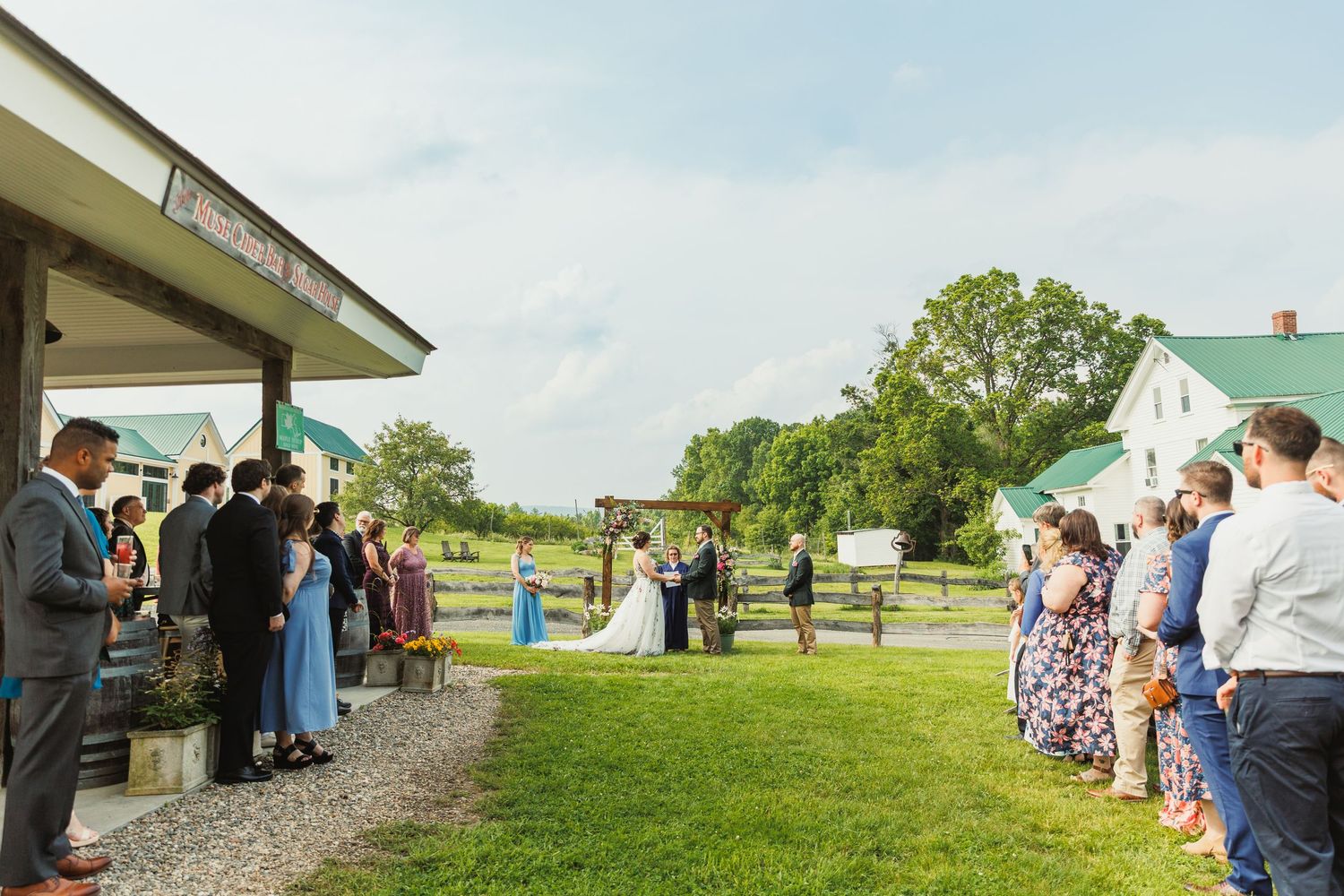 Wedding guests line up along a gravel path with rolling hills and farmland in the background.