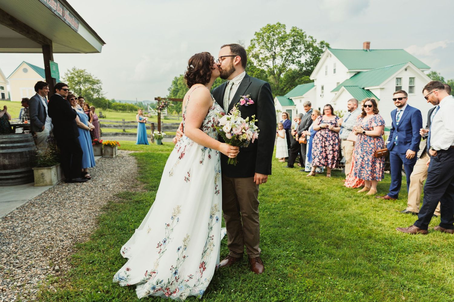 Wedding ceremony procession on gravel path with guests watching from wooden chairs.