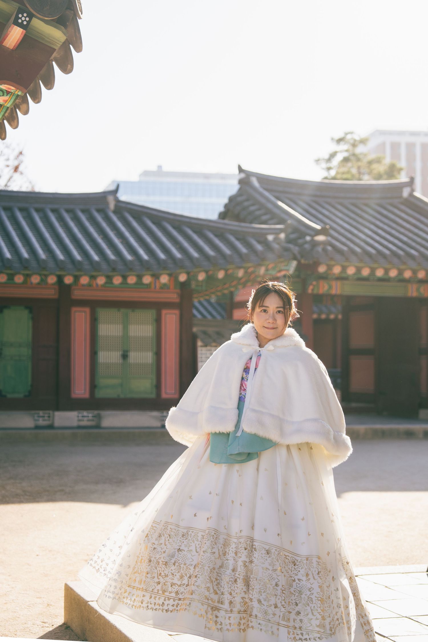 Traditional Korean hanbok dress with flowing white layers photographed at a historic palace courtyard in sunlight.