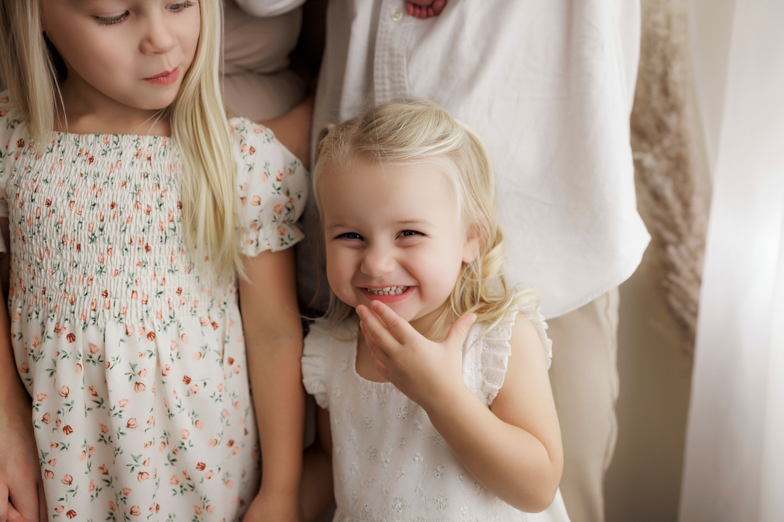 A young child in a floral dress stands against a white backdrop while looking away from the camera.
