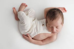 Peaceful sleeping newborn baby in white clothing curled up on light background in artistic collage composition.