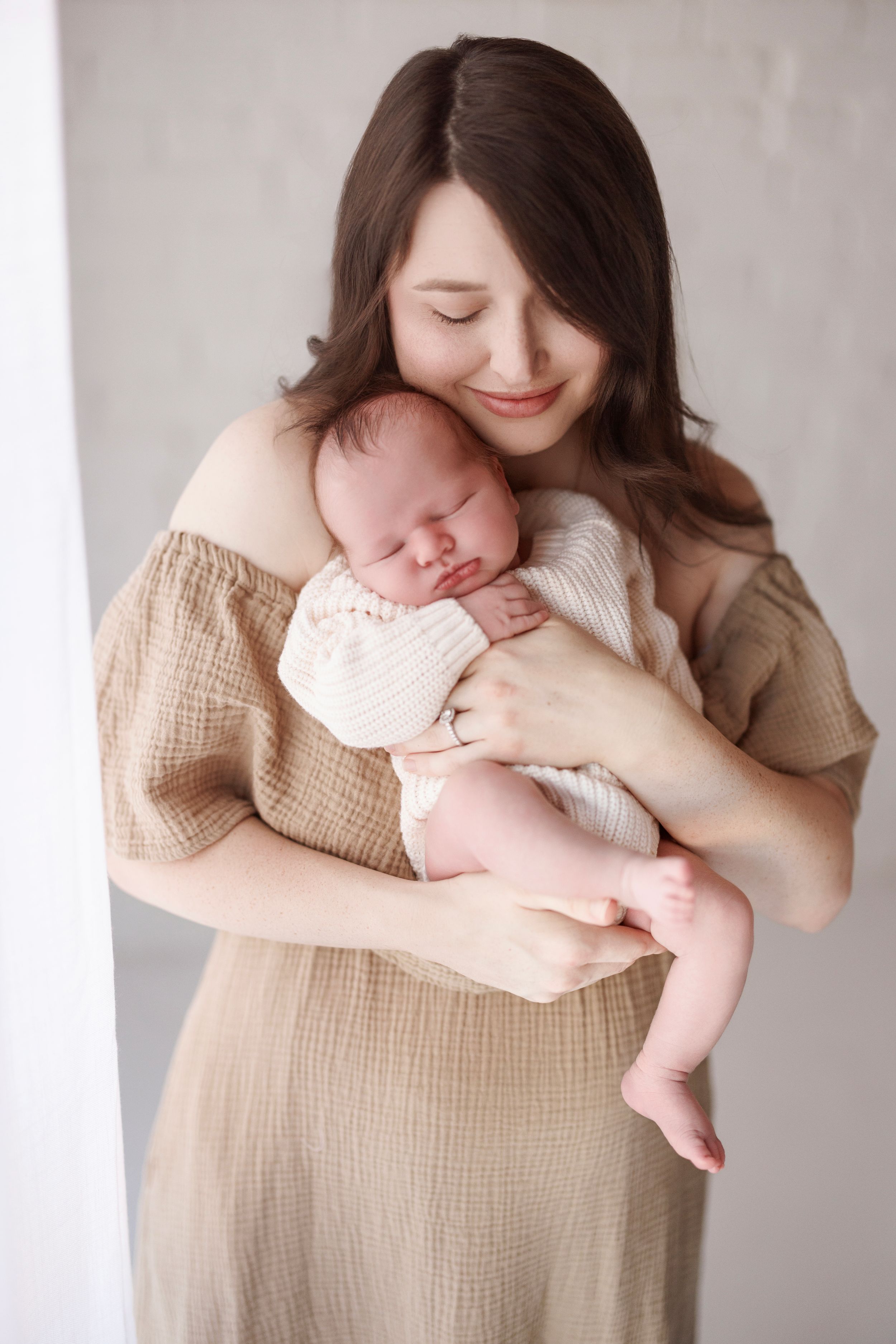A tender series of photos showing a parent in beige linen clothing gently cradling and embracing their newborn baby.