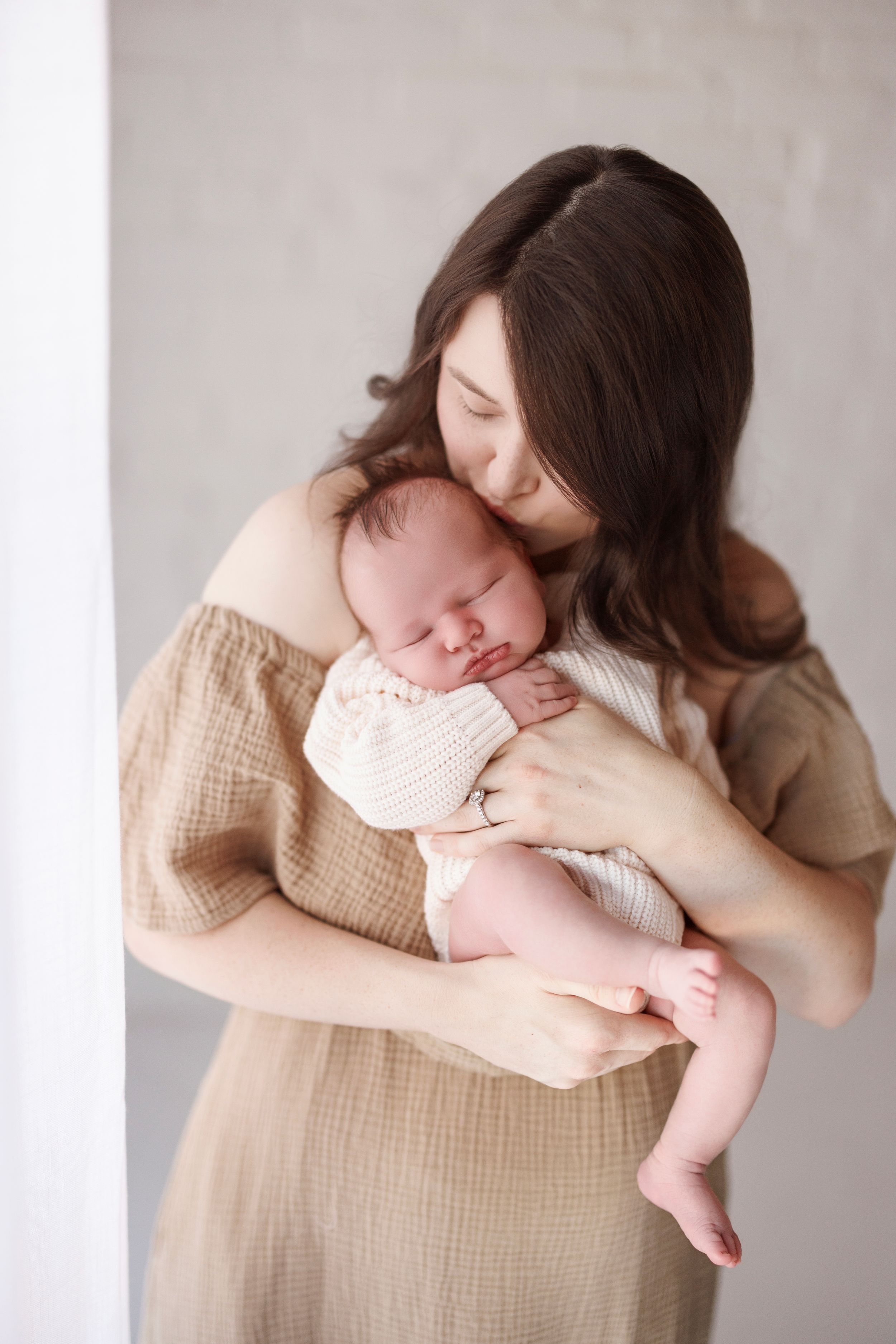 A tender moment captured in soft beige tones as a mother cradles her sleeping newborn baby in a gentle embrace.