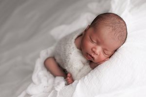 Sleeping newborn baby wrapped in soft white blanket rests peacefully during professional photo session.