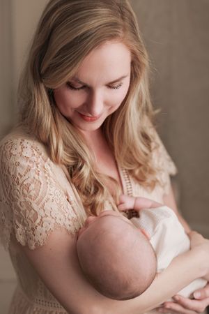 A tender moment captured in soft lighting as a mother in a white lace dress cradles and nurses her newborn baby.