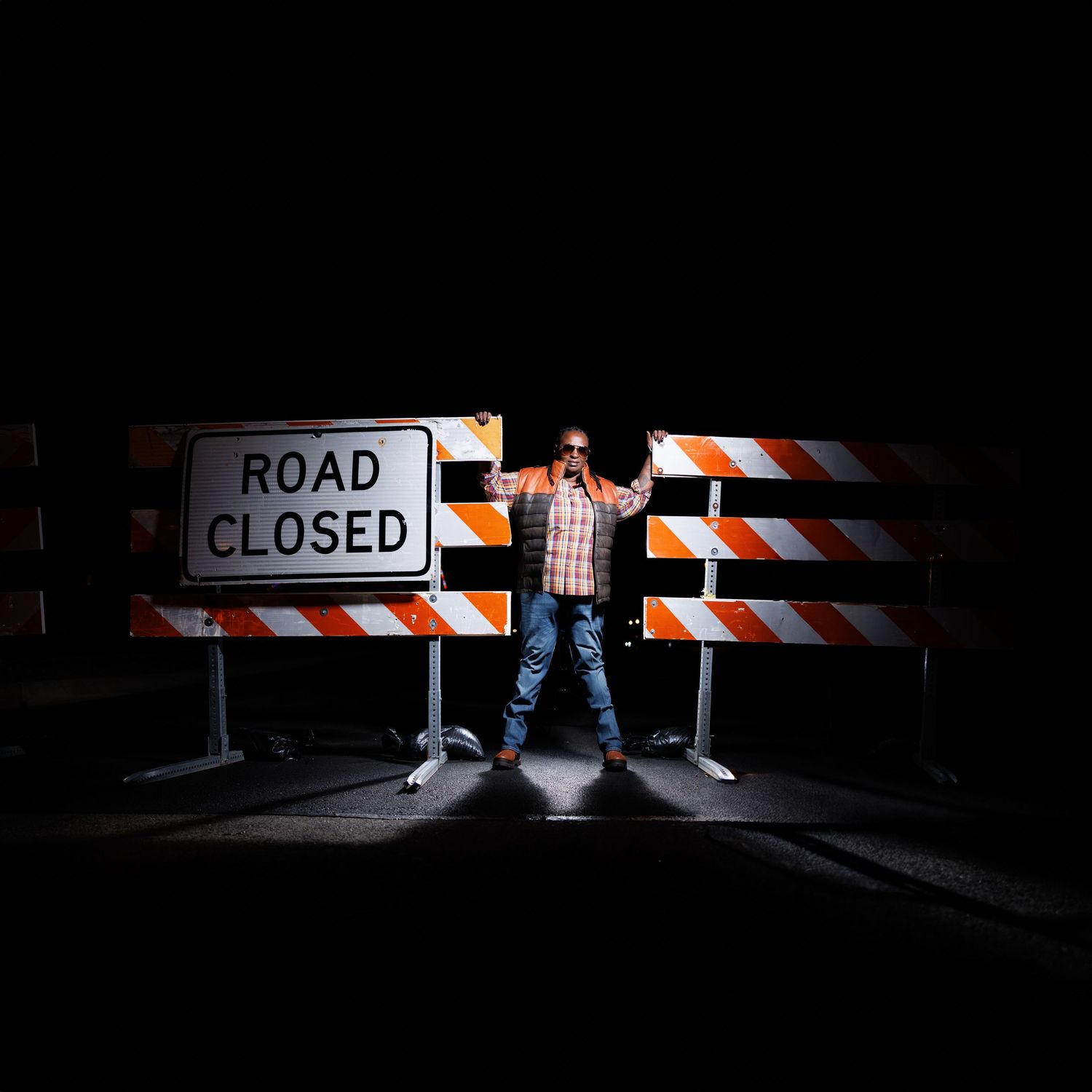 Road closed barricade illuminated in darkness with person's legs visible.
