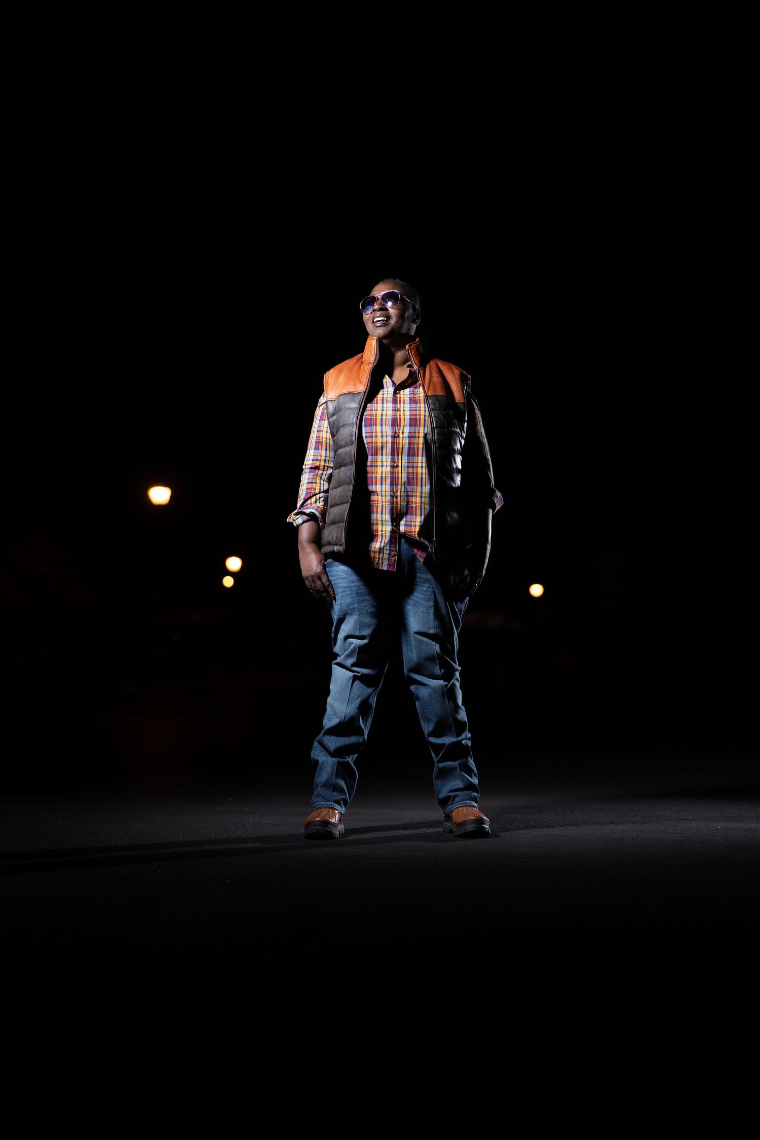 Worker in reflective vest and jeans stands illuminated in dark space.