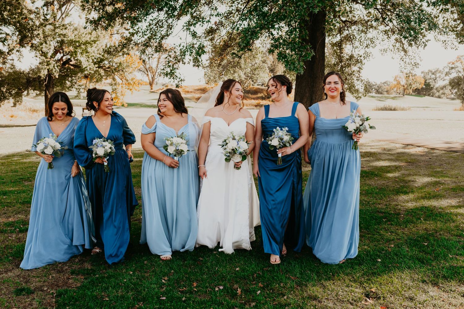 Wedding party poses on the rolling green hills of the golf course, warm fall colors stretching across the background under a soft sunset