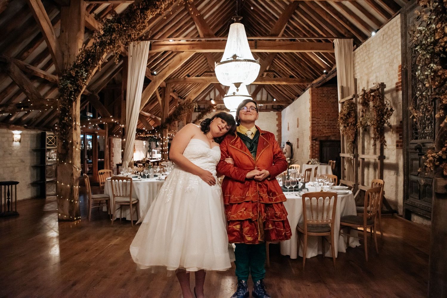 Wedding couple at a rustic barn wedding reception venue with exposed wooden beams and chandeliers.