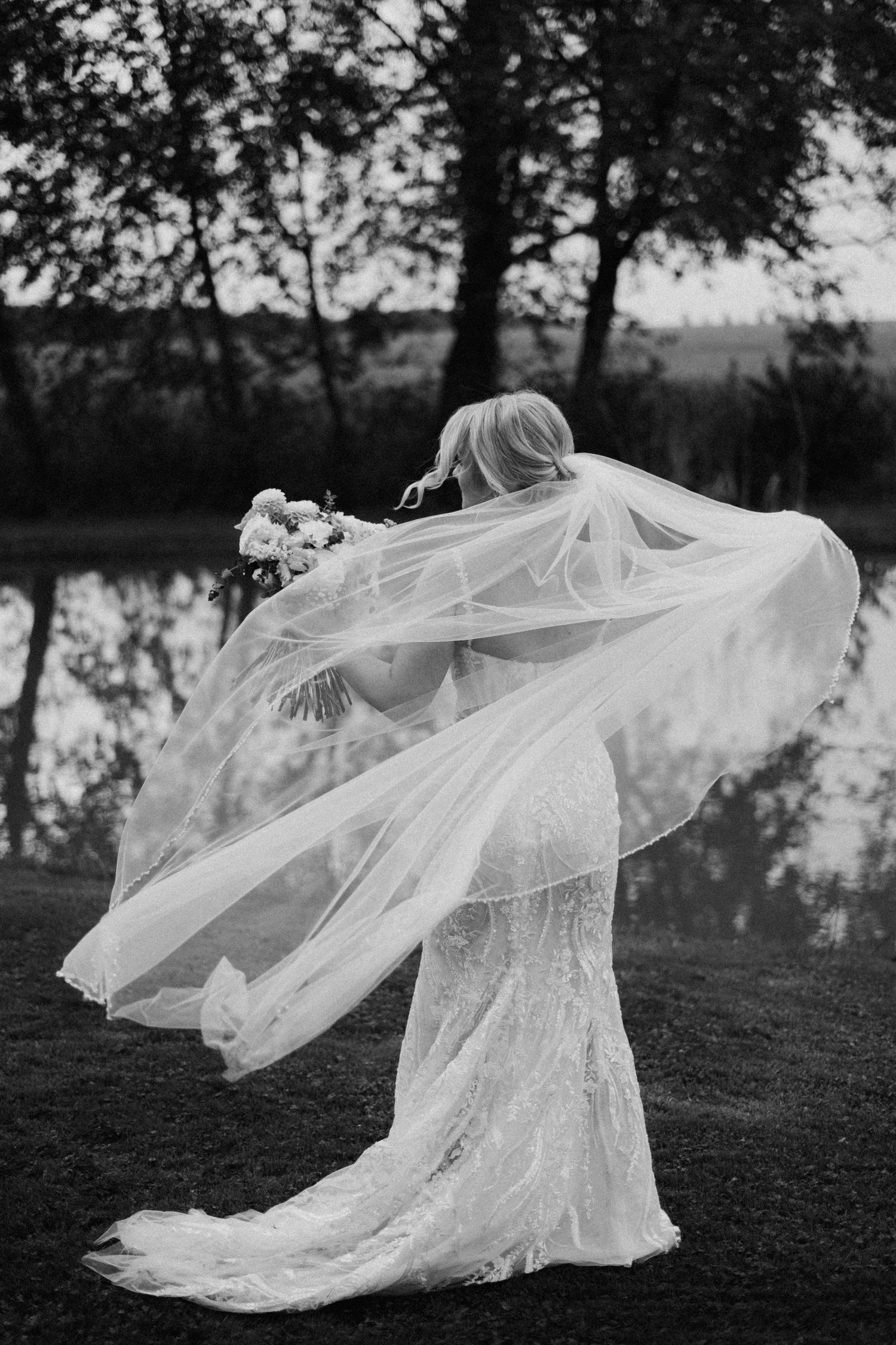 A flowing white lace wedding dress and veil catch the breeze in a dramatic black and white outdoor portrait series.