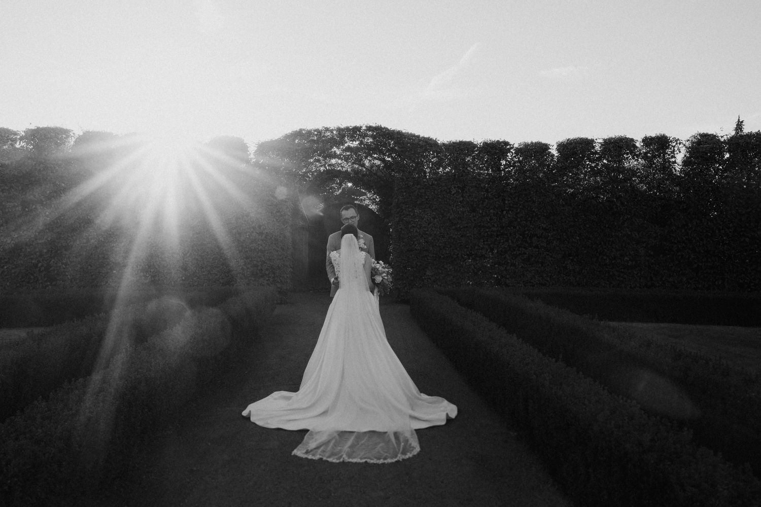 Dramatic black and white wedding photo with sunburst effect behind flowing bridal gown.