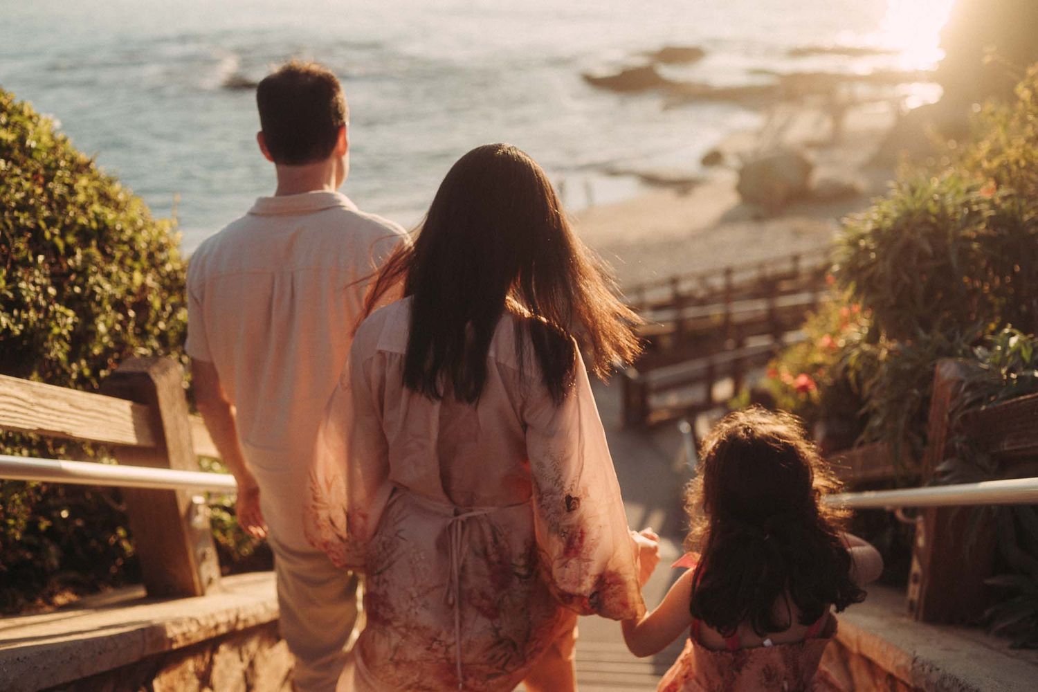 Two people walk along a scenic coastal path during golden hour sunset by the ocean.