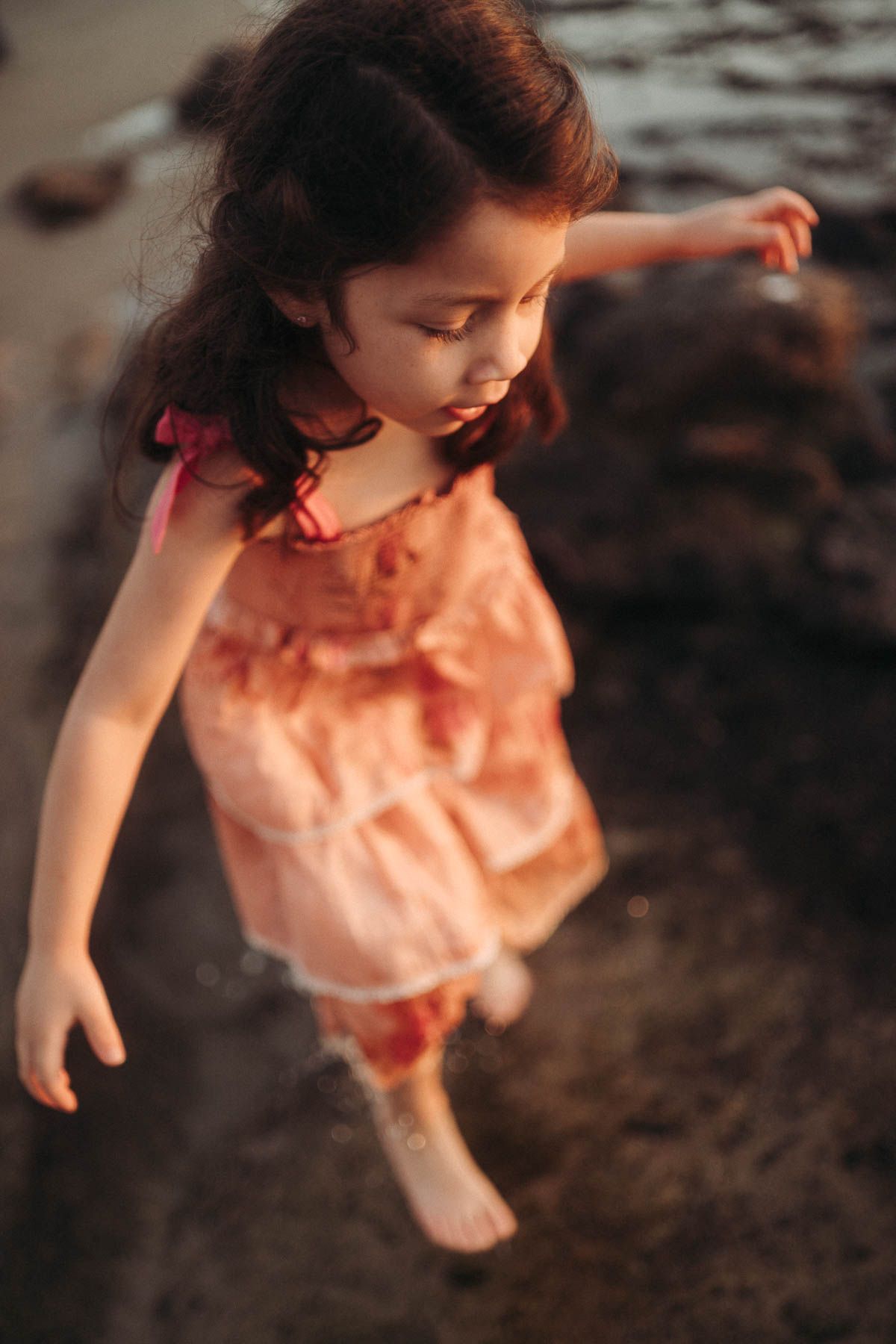 A small doll wearing a peach-colored dress stands against a dark background.