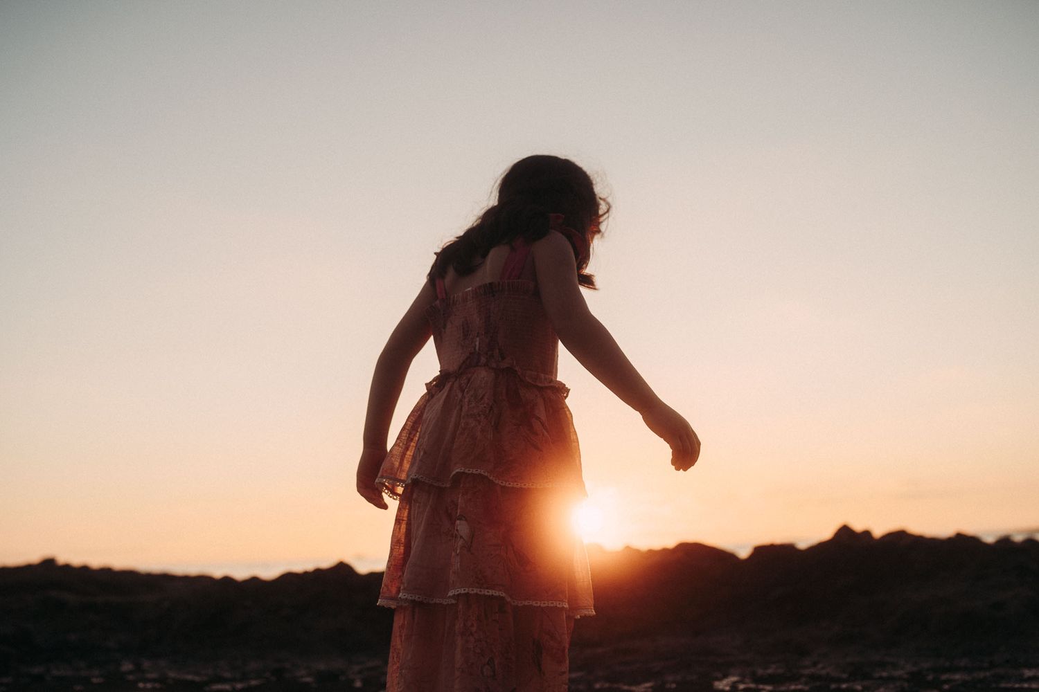 Silhouettes of people walking along rocky beach shore during dramatic orange sunset.