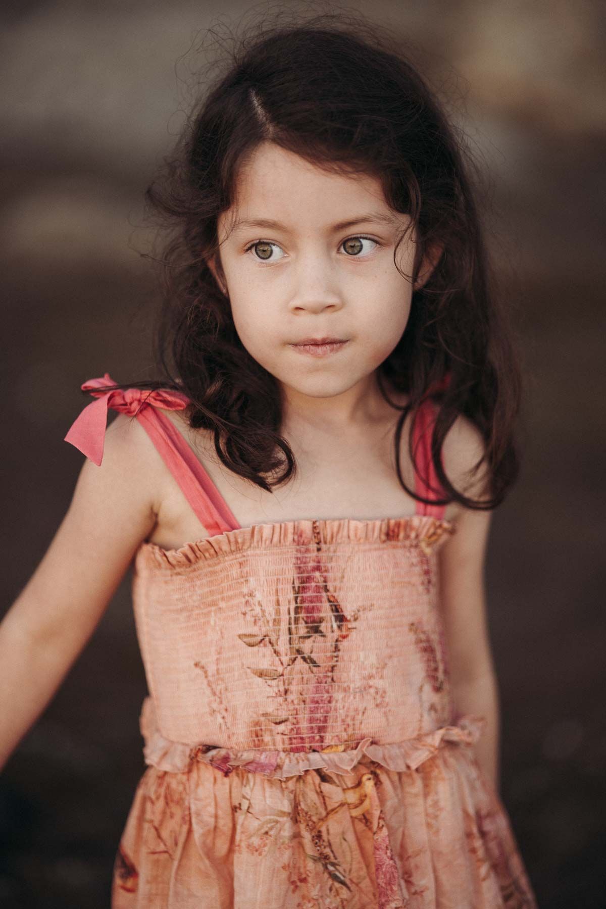 Young child wearing a peach-colored smocked dress with ruffled straps against a dark background.
