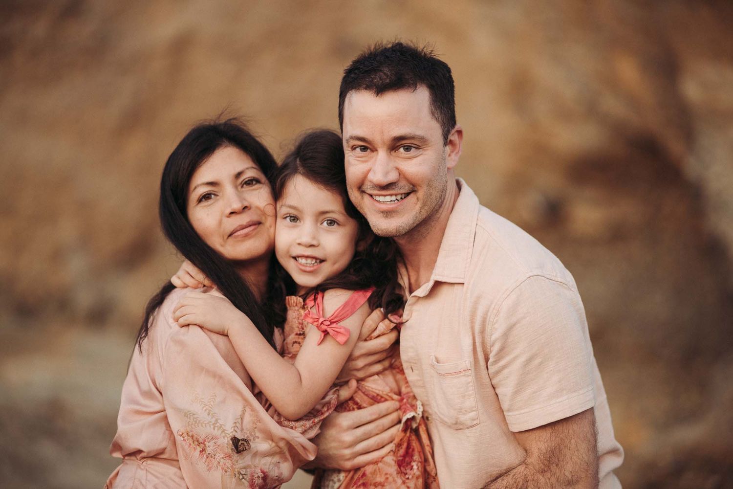 A family poses together outdoors for a portrait against a blurred brown background.