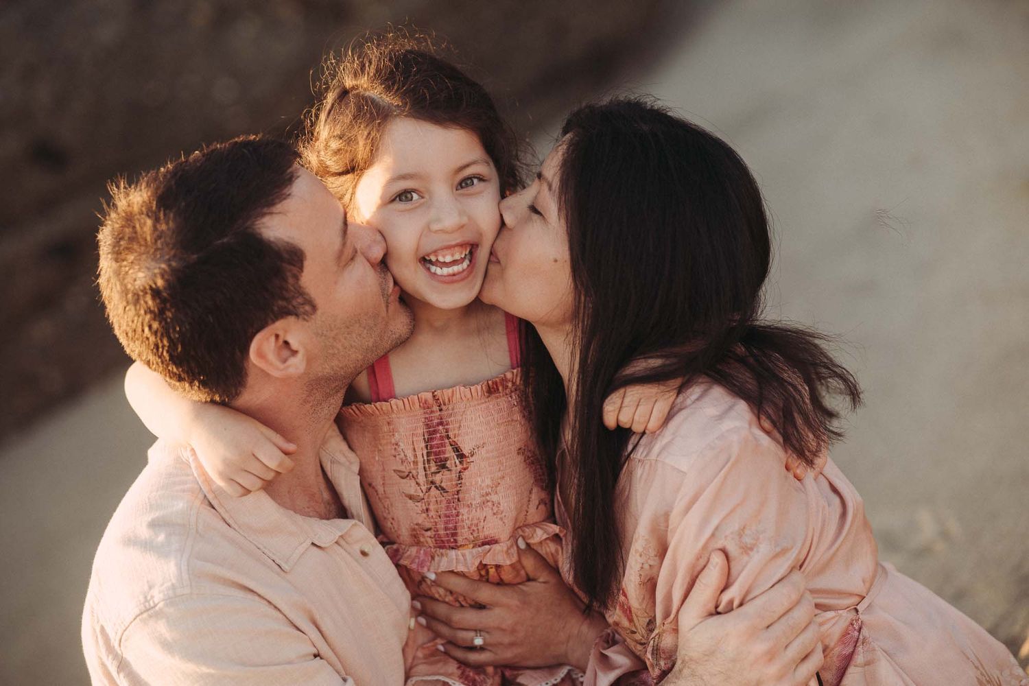 A loving family shares tender moments together in a series of intimate portraits wearing soft pink and neutral tones.