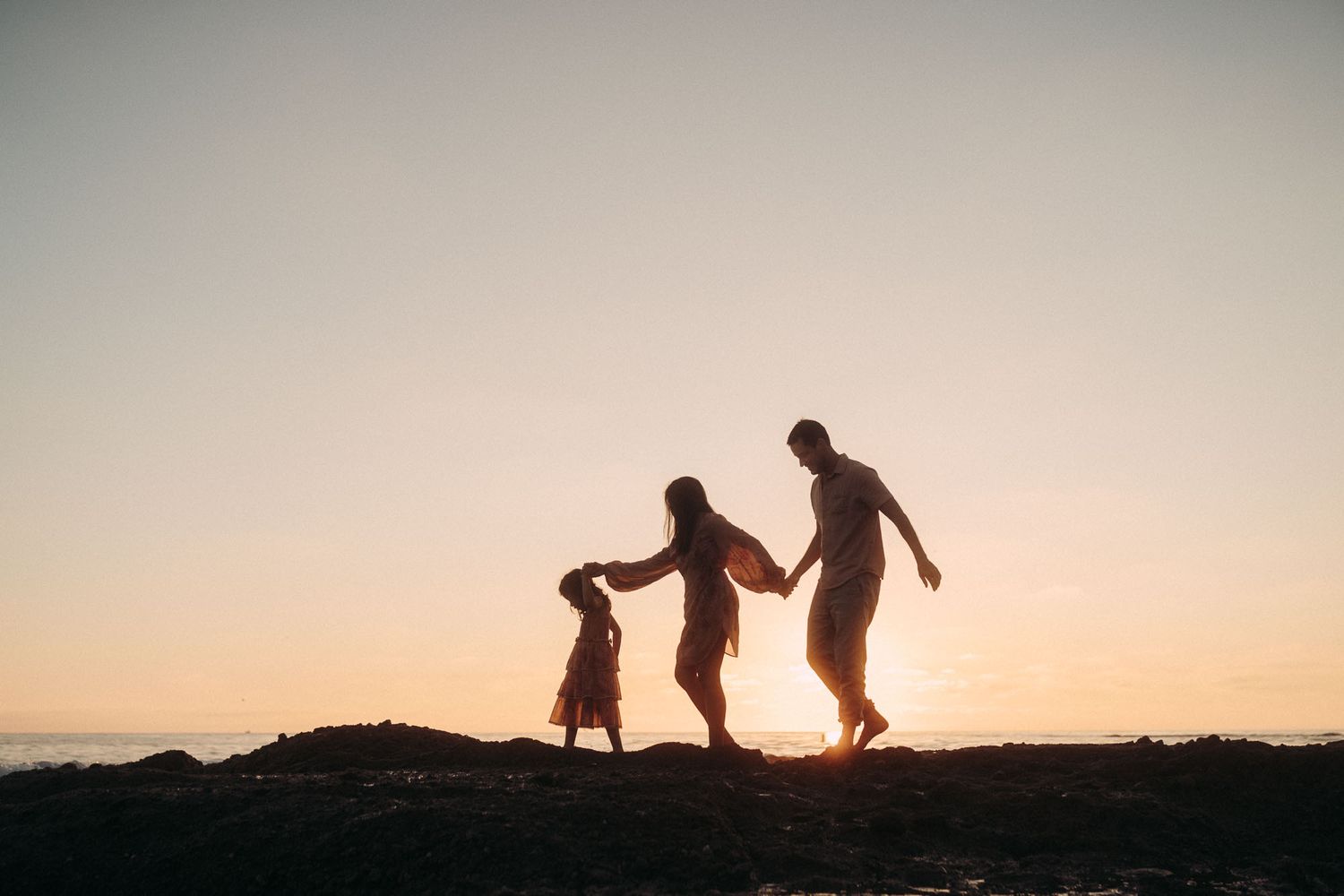Silhouettes of people walking along a beach at sunset with warm orange and purple sky in the background.