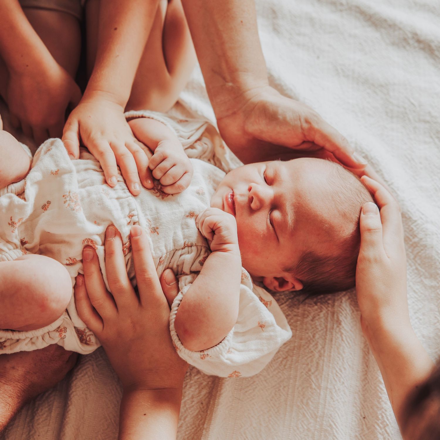 New born baby with the rest of the families hands around her.
