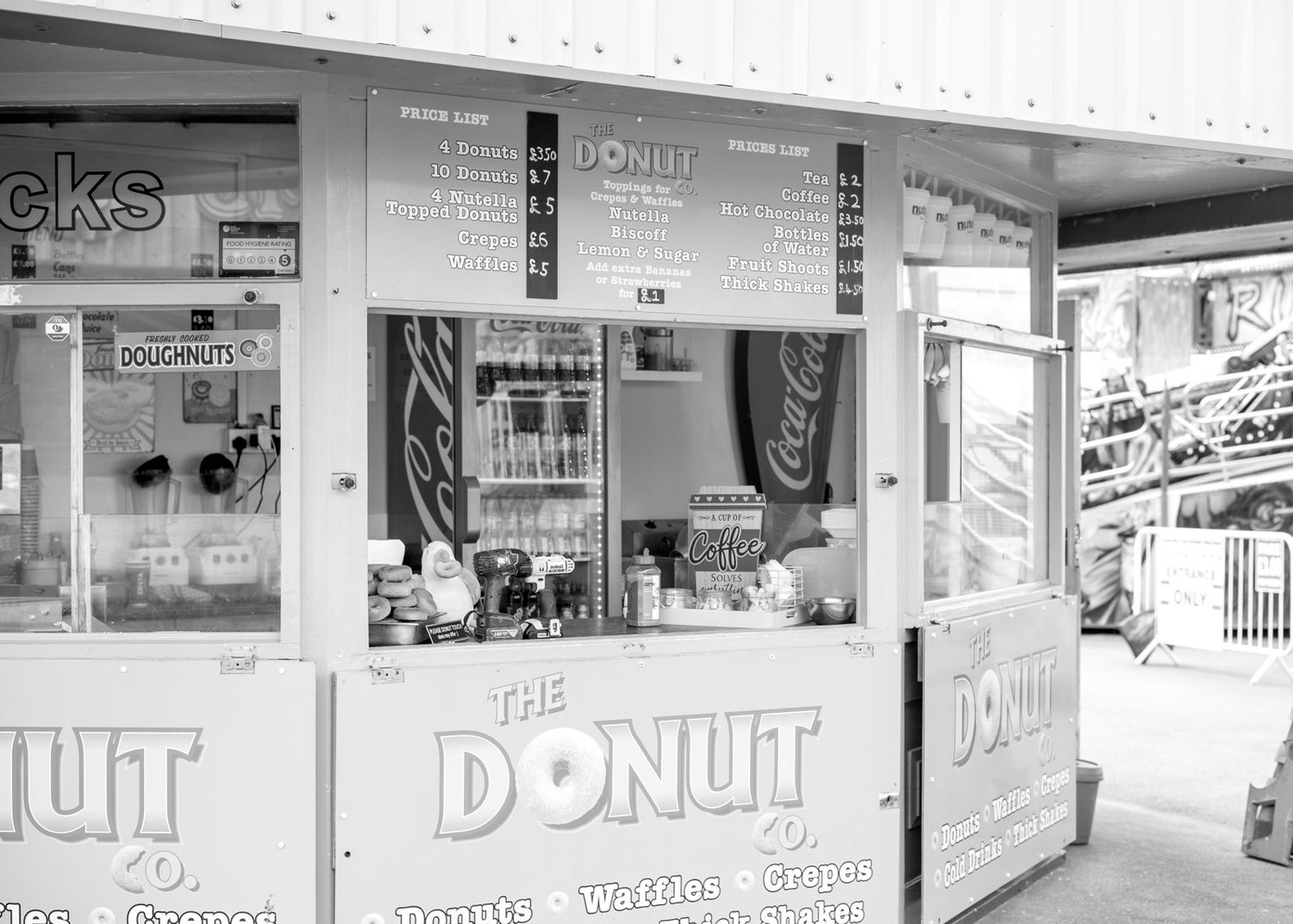 Black and white storefront view of a donut shop with signage and display windows along a commercial strip.