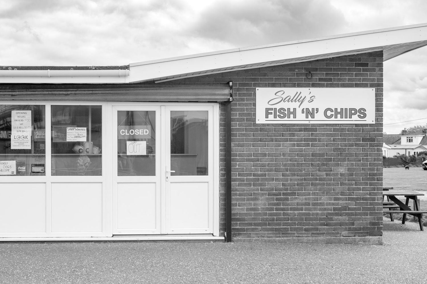 Black and white photo of a vintage brick fish and chips shop storefront with white doors and windows.