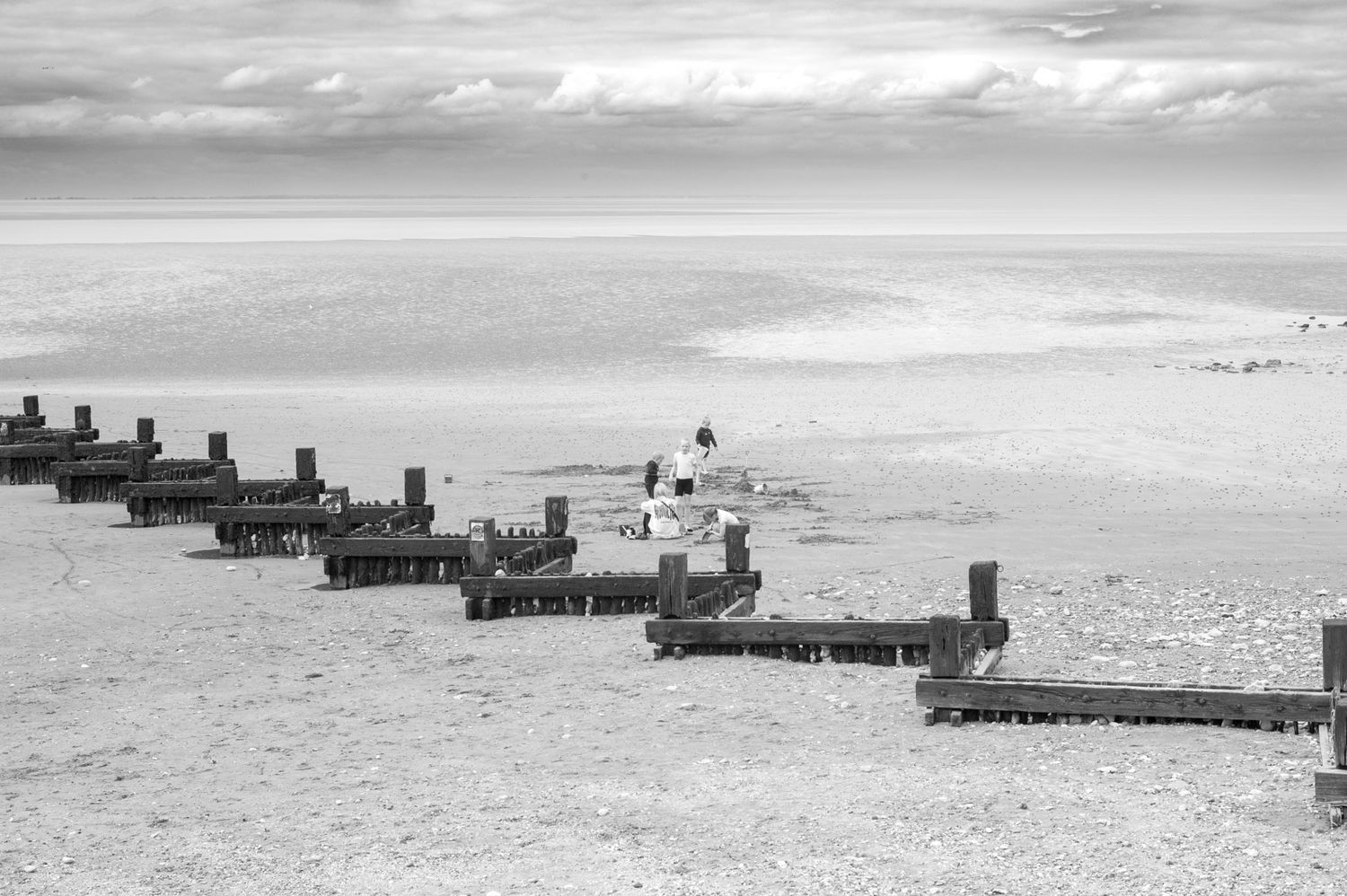 Row of wooden jetty posts extending into a misty ocean under an overcast sky.