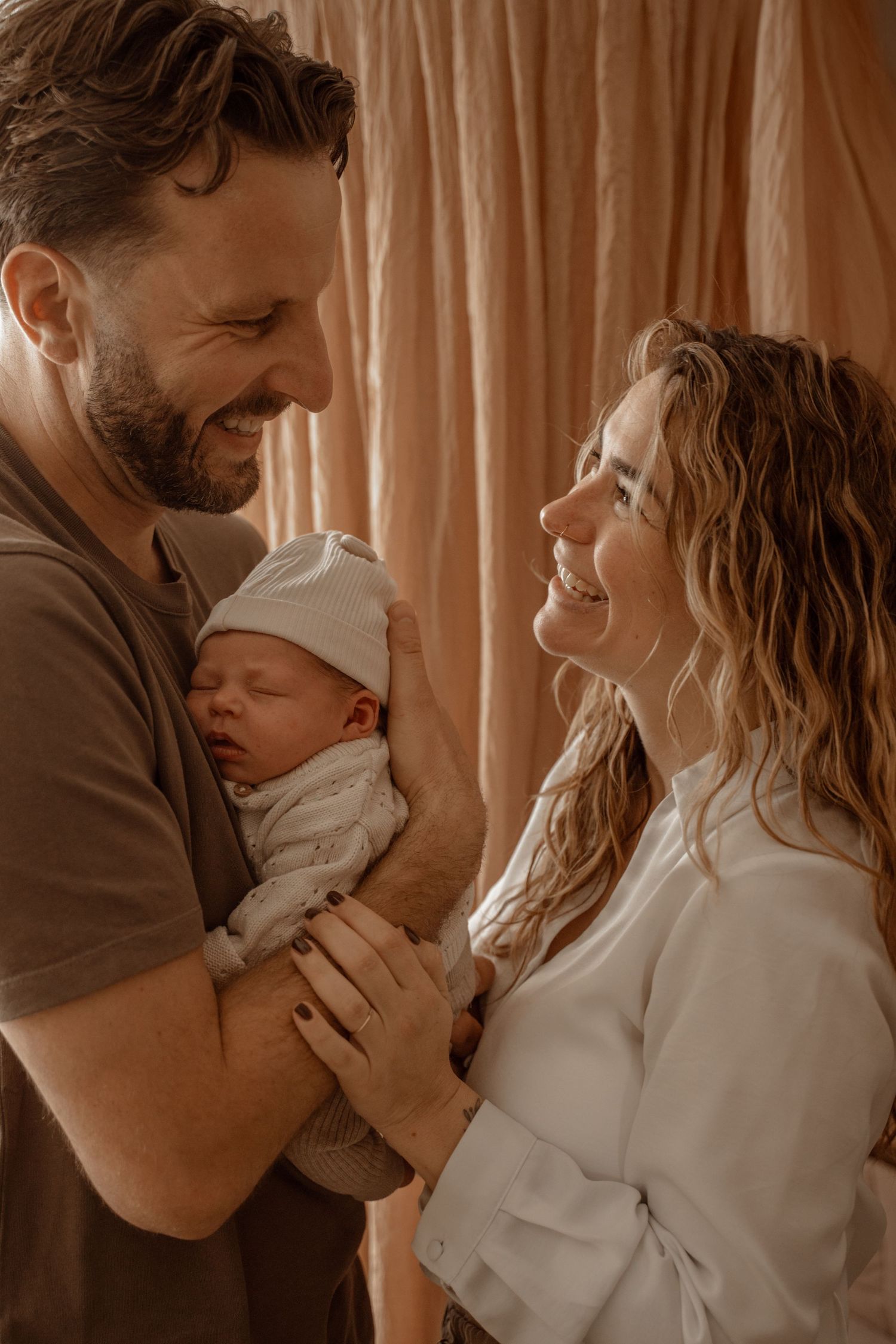 A loving family moment captured in warm tones as parents embrace their newborn baby in a tender photoshoot series.