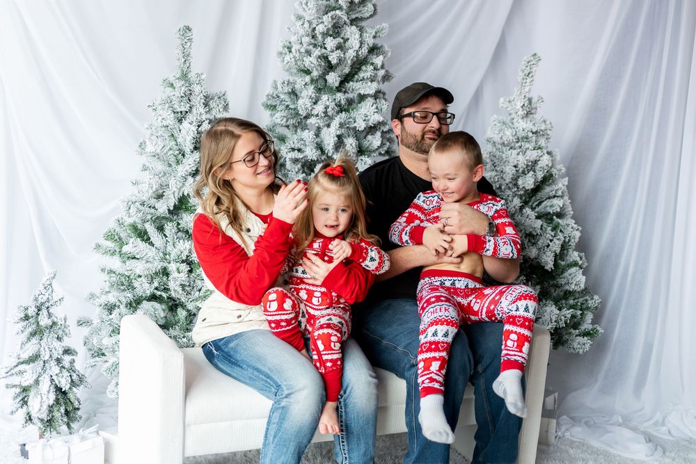 Family with two young children in matching red Christmas pajamas on white bench.