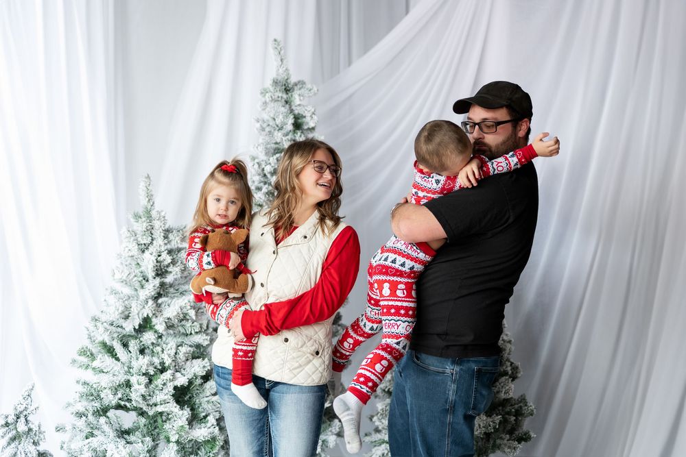 Family of four in matching red Christmas pajamas posing with snowy holiday trees.