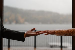 Two hands reaching out towards each other against a blurred natural background with mountains and water.