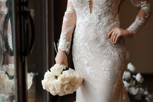 A bride in a lace wedding dress holds a white and cream bouquet in an elegant indoor setting.