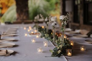 Wedding reception table settings with candlelight and greenery create an elegant ambiance at dusk.