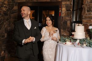 Wedding reception scene in a rustic stone-walled venue with elegant table settings and a white cake display.