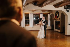Newlywed couple dances together in an elegant indoor venue with wooden beams and warm lighting.