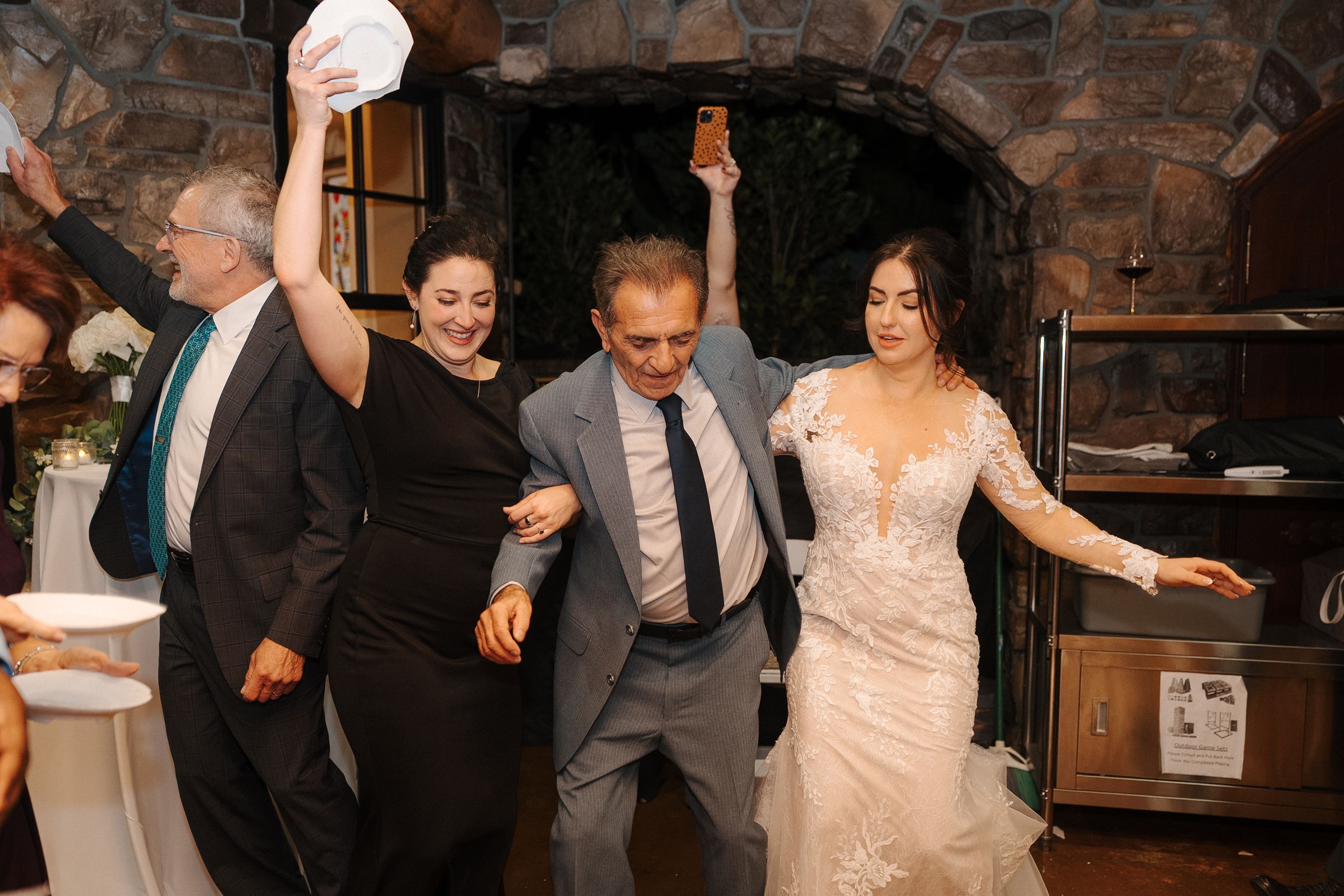 Wedding guests dance and celebrate on a rustic stone-walled dance floor during a reception party.